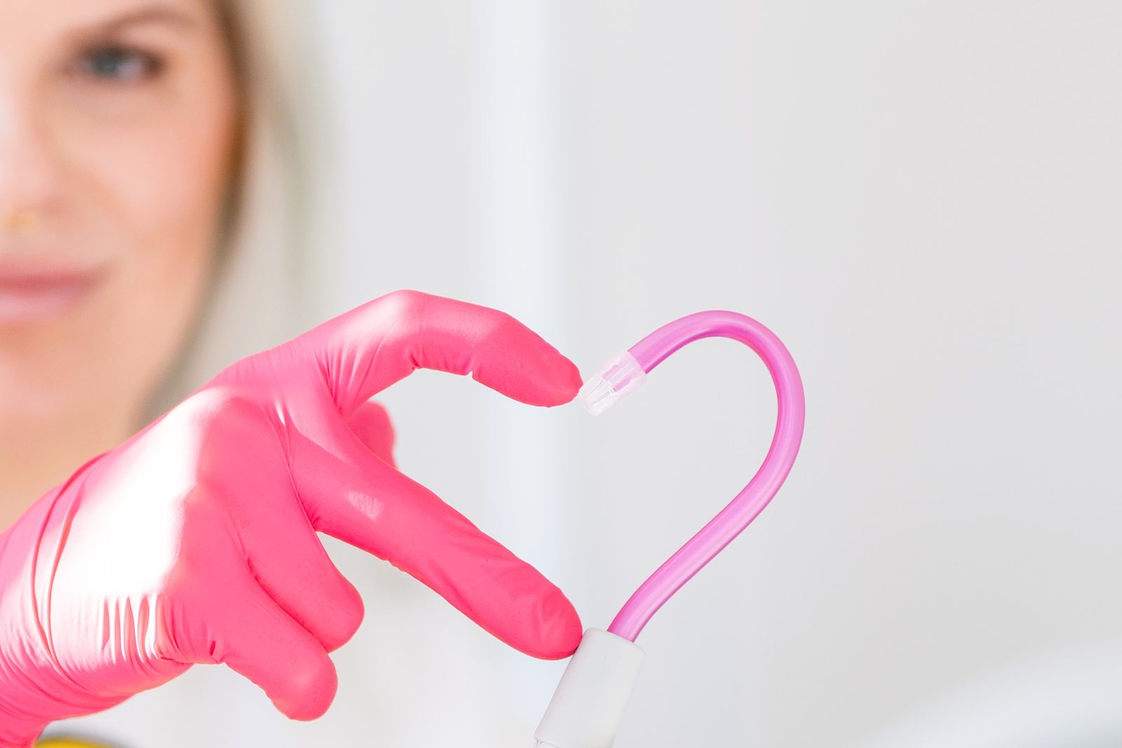 Mitarbeiterin formt mit rosa Handschuh und Sauger ein Herz
